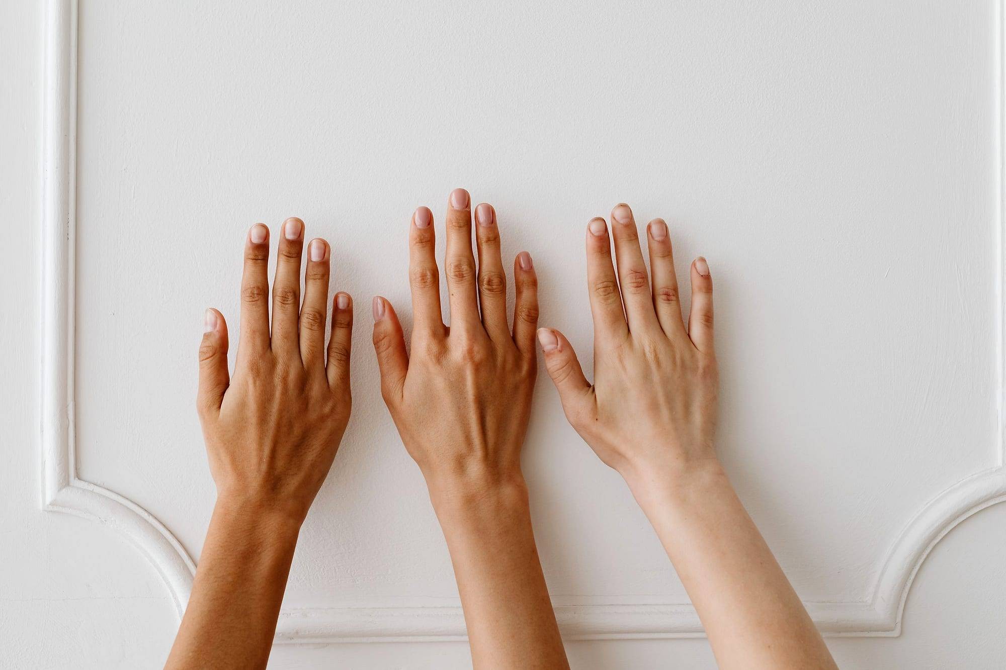 Tres manos con distintos tonos de piel apoyadas sobre una pared blanca