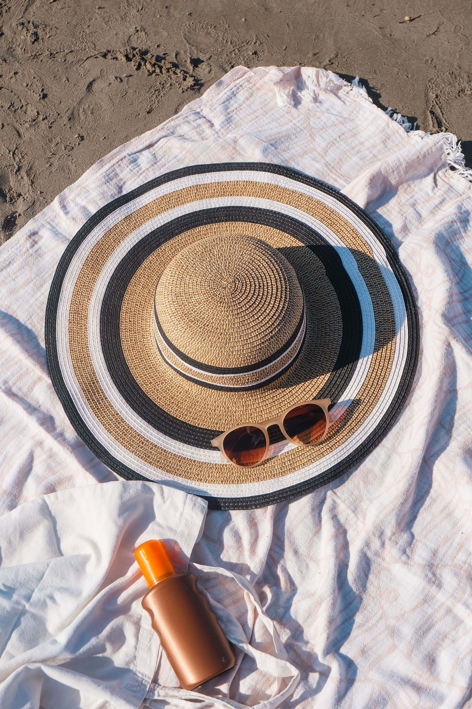 Sombrero de paja, gafas de sol y protector solar sobre una toalla blanca en la playa