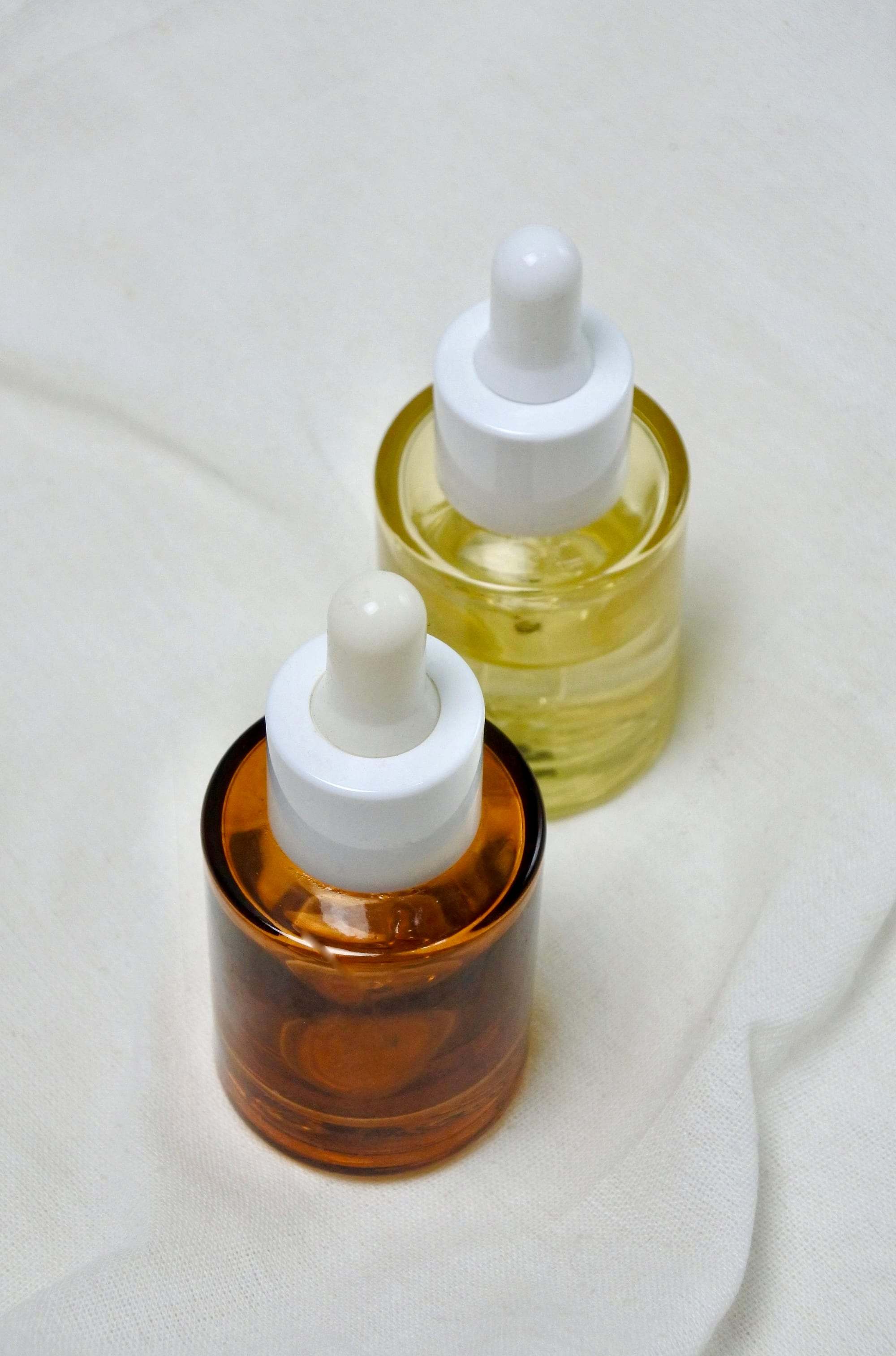 Dos frascos de sérum con cuentagotas, uno ámbar y otro dorado, sobre fondo claro