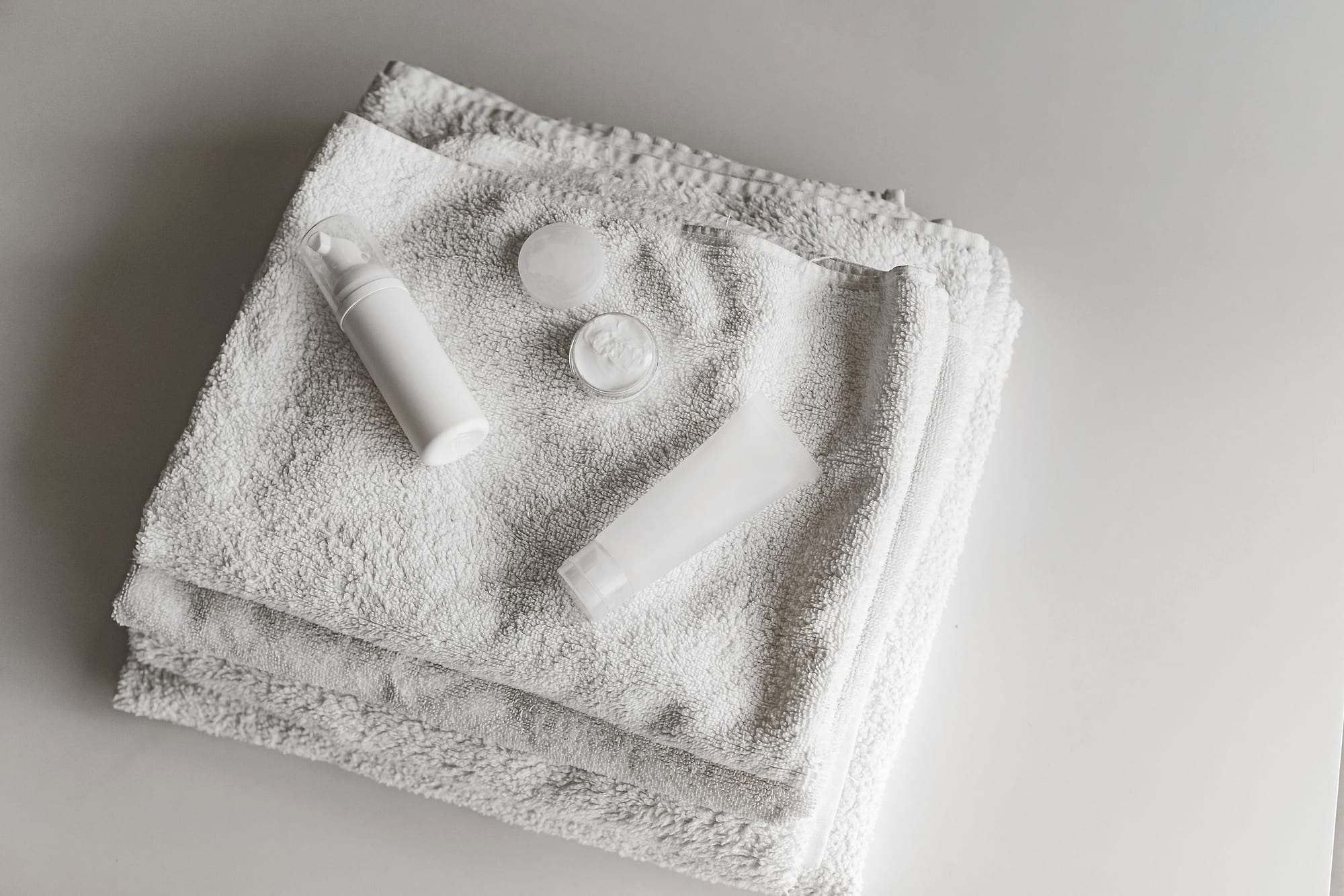 Toallas blancas dobladas con envases cosméticos blancos en una composición minimalista