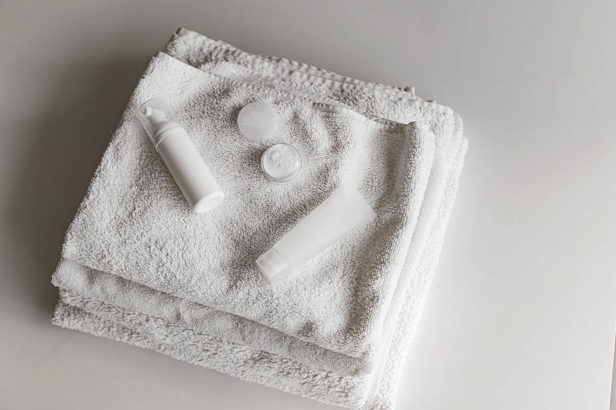 Folded white towels with white skincare containers in a minimalist composition