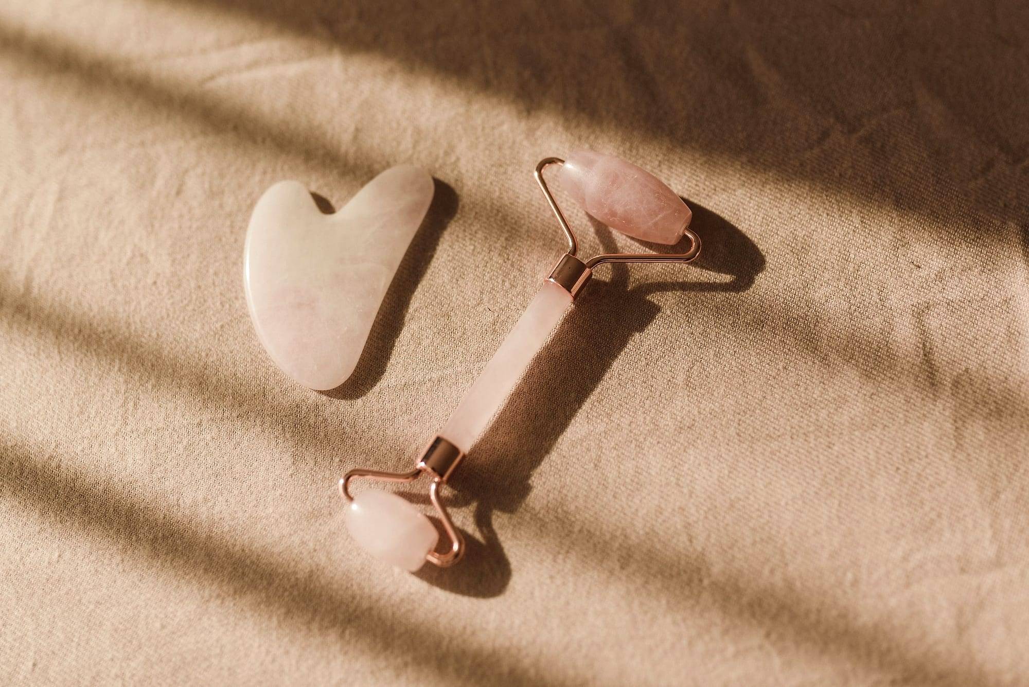 Rose quartz facial roller and gua sha stone on beige fabric in soft light