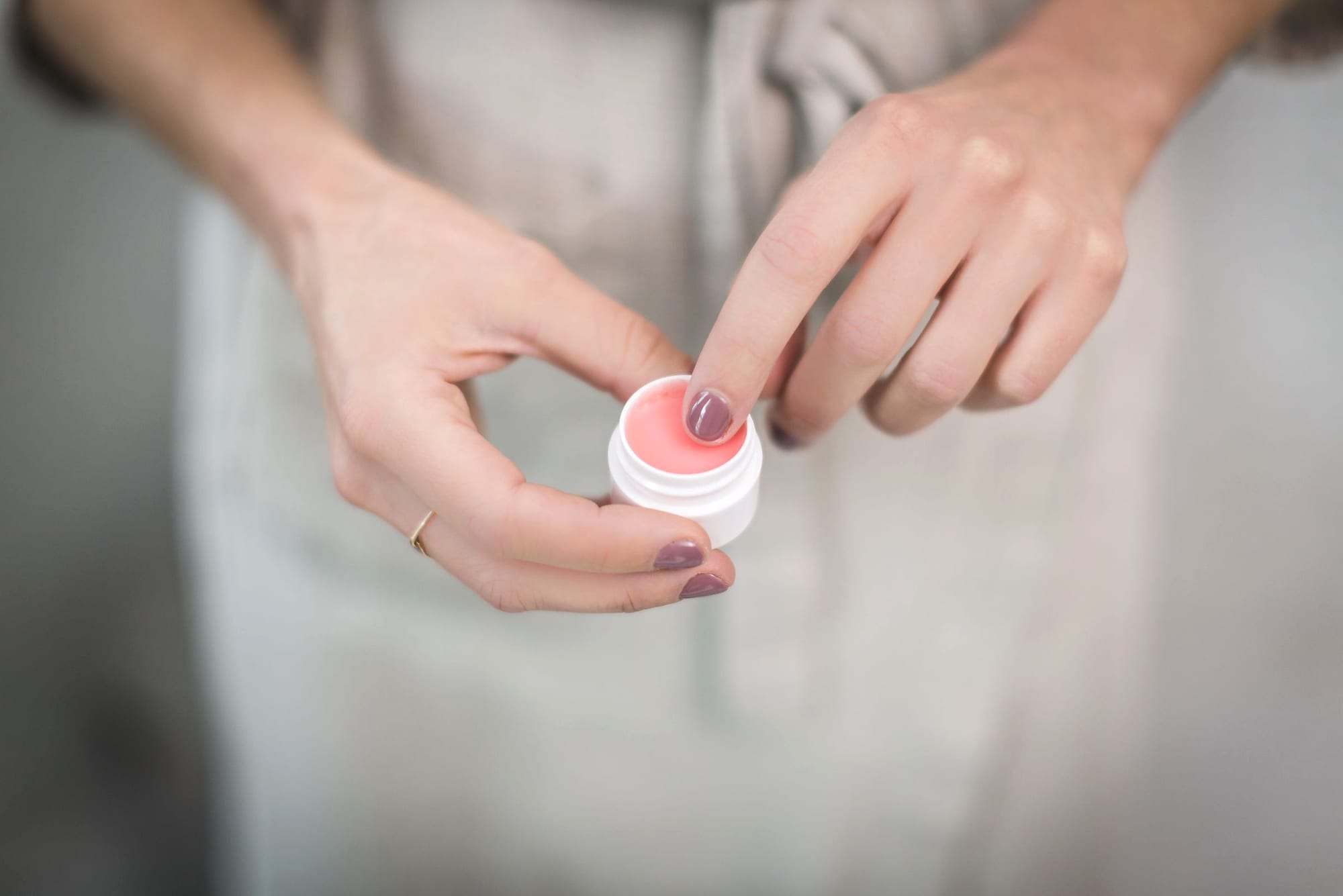 Manos abriendo un pequeño tarro de bálsamo labial rosa
