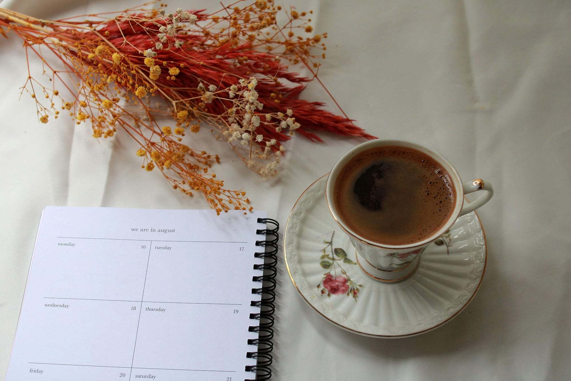 Agenda abierta junto a una taza de café y flores secas sobre un lino claro