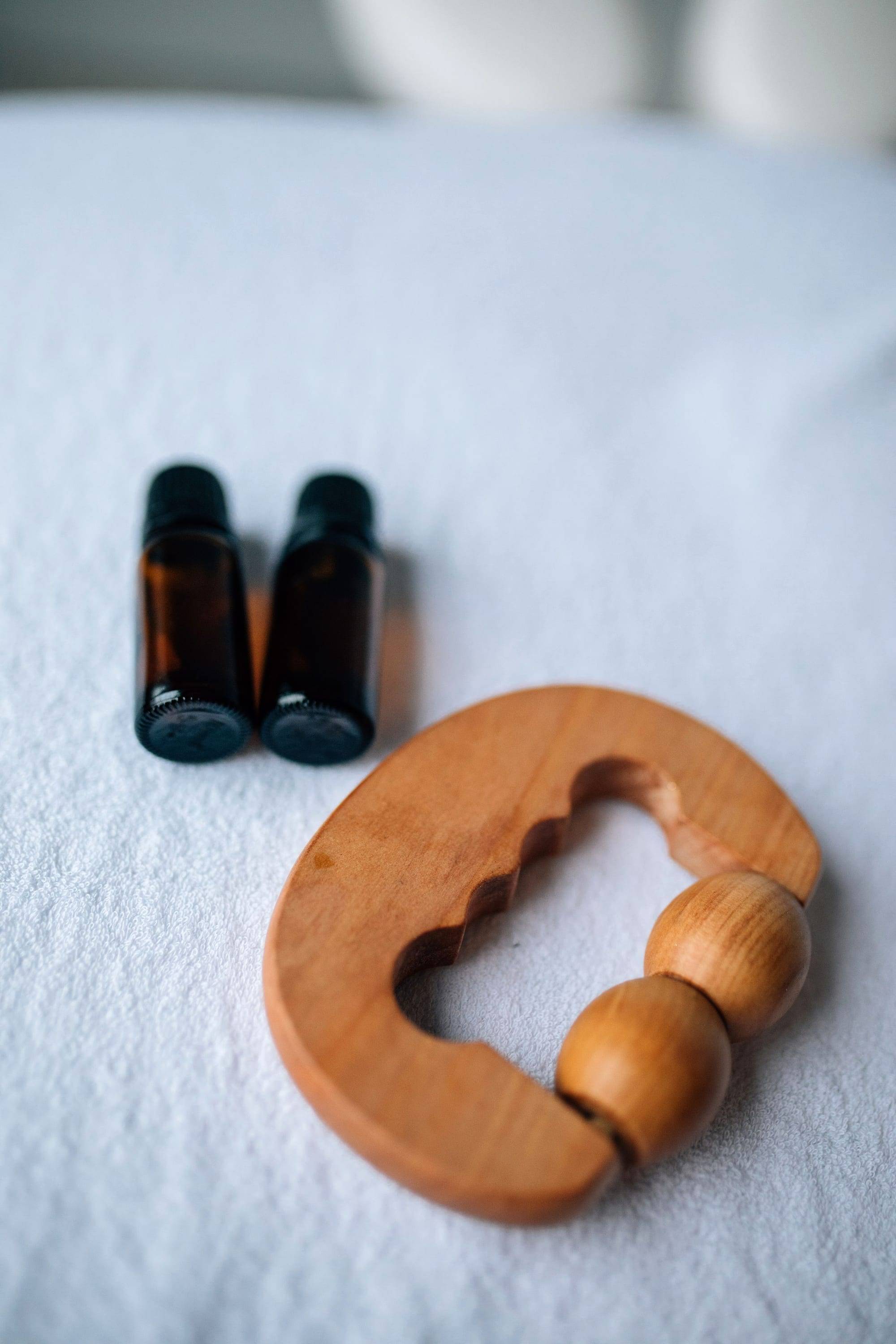 Wooden massage tool beside two essential oil bottles on a white towel