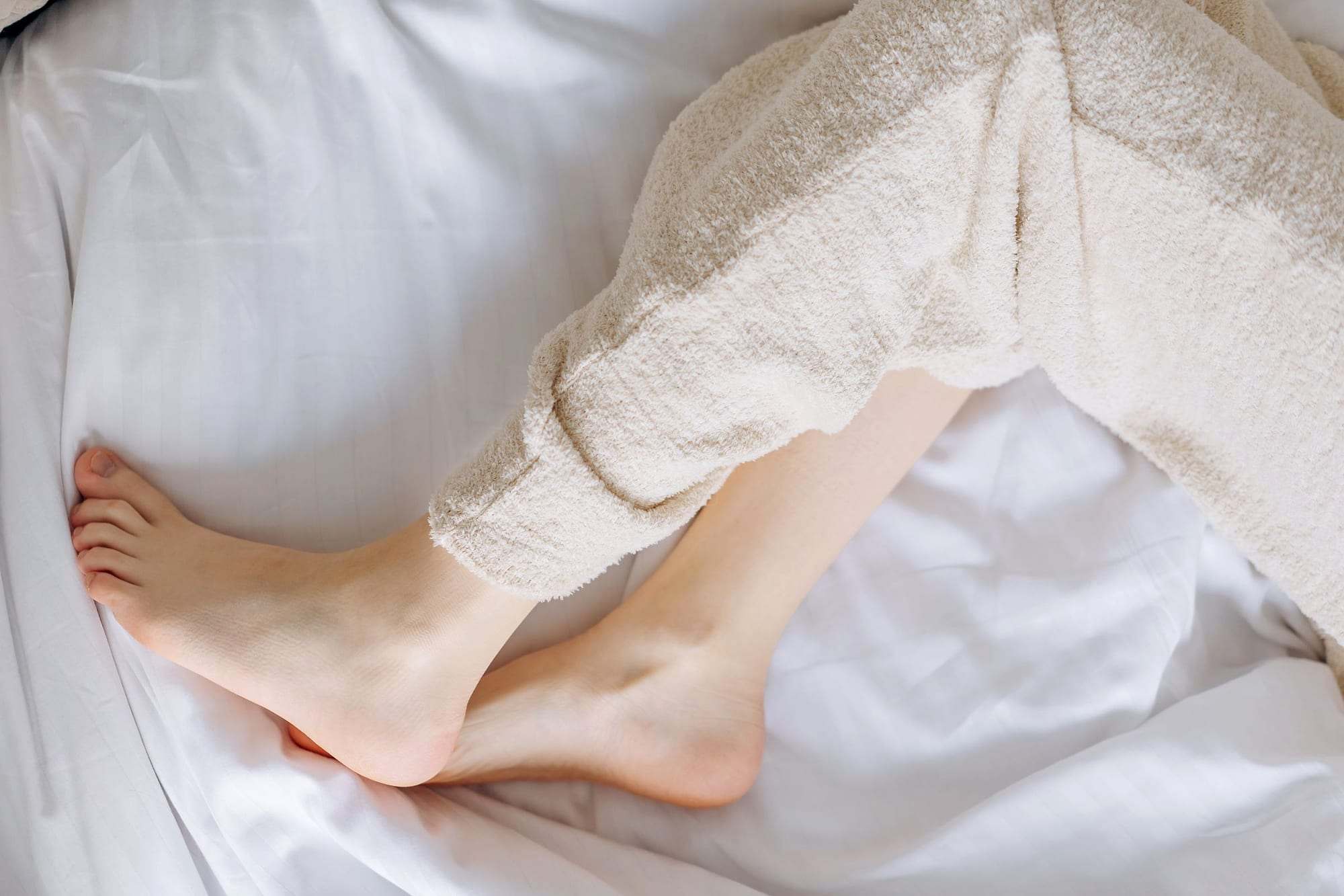 Piernas relajadas descansando sobre unas sábanas blancas