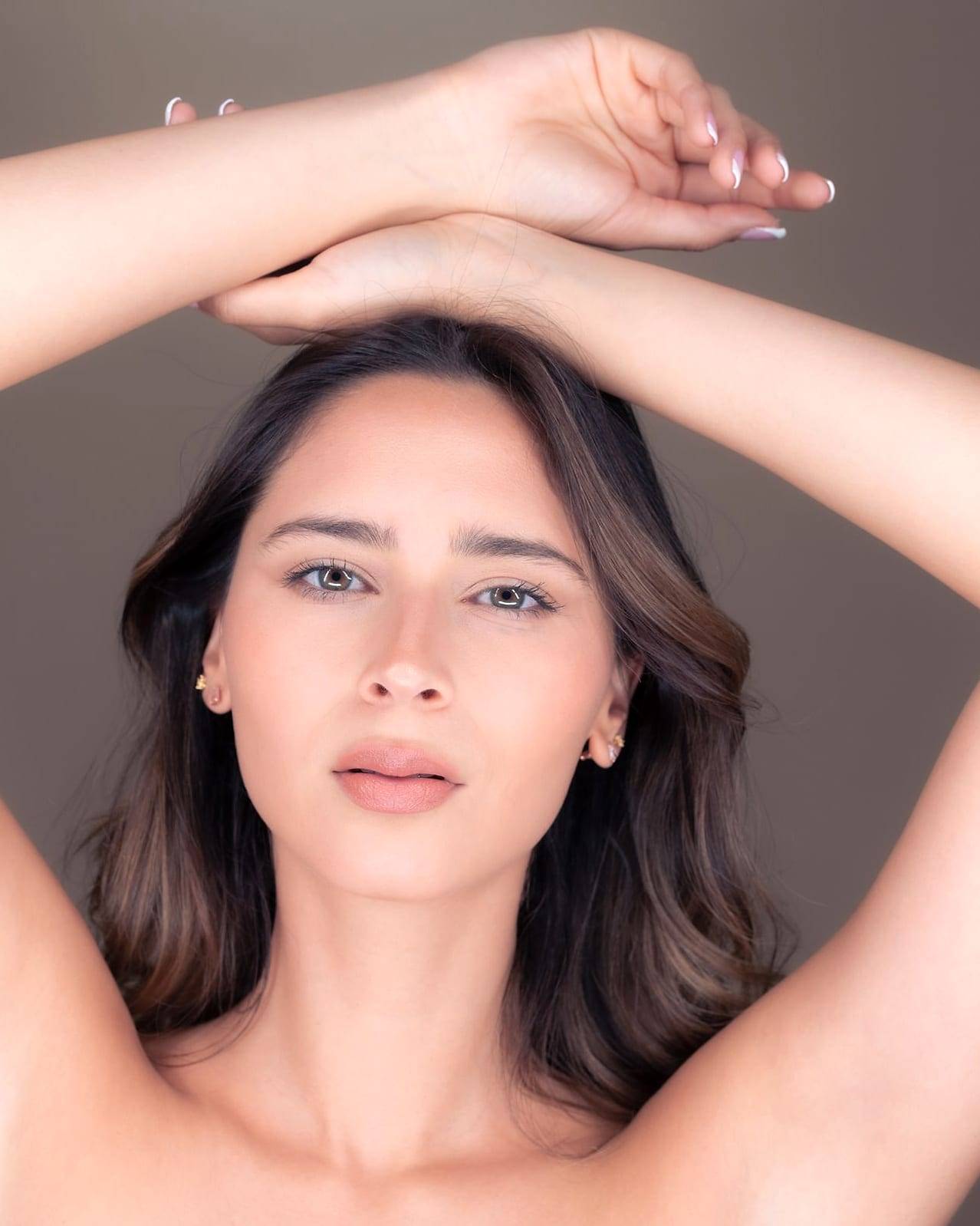 Mujer morena con los brazos levantados sobre la cabeza y las axilas lisas, sobre un fondo cálido