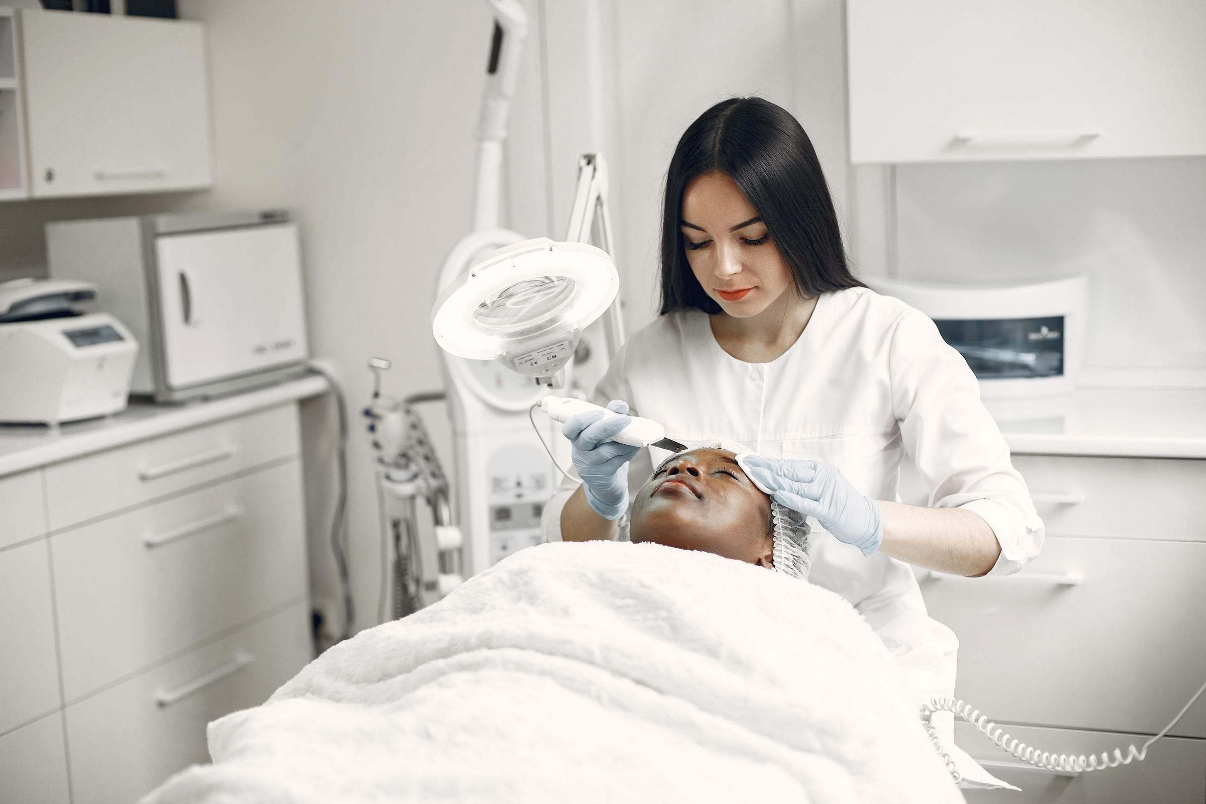 Esteticista realizando una limpieza facial con lupa en una cabina blanca