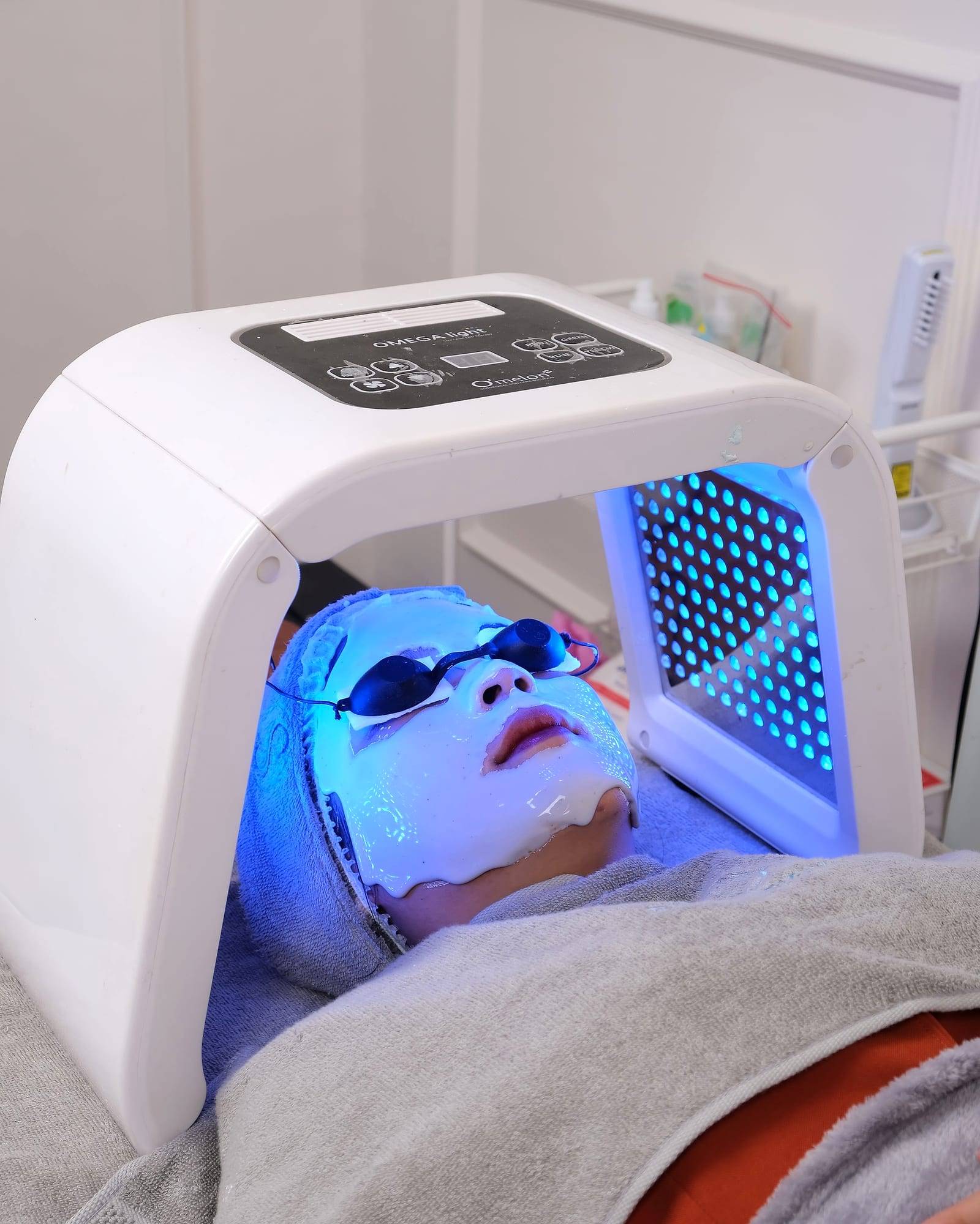 Clienta bajo un panel de fototerapia LED azul durante un tratamiento facial